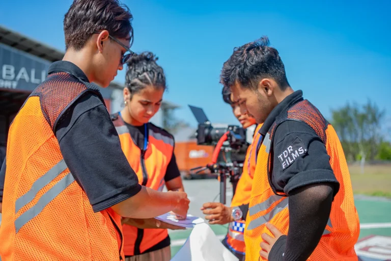 TDR FILMS crew in orange safety vests reviewing production notes at the heliport before a TVC shoot, Bali